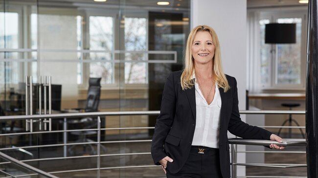 Isabella Leßwing Isabella Leßwing – Mitglied im Führungsteam der offino Bürolösungen GmbH – posiert in dunkler Geschäftskleidung und sympathisch lächelnd vor dem Treppenabgang im ersten Stock des offino Showrooms in Kempten