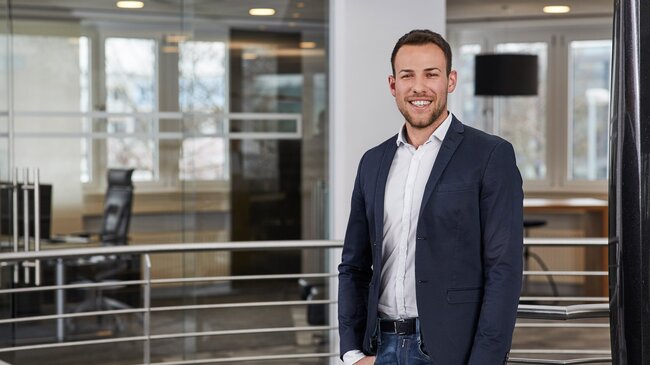 Fabio Leßwing Fabio Leßwing – Mitglied im Führungsteam der offino Bürolösungen GmbH – posiert in dunkler Geschäftskleidung und sympathisch lächelnd vor dem Treppenabgang im ersten Stock des offino Showrooms in Kempten