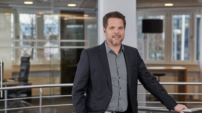 Jörg Wegmann Jörg Wegmann – Mitglied im Führungsteam der offino Bürolösungen GmbH – posiert in dunkler Geschäftskleidung und sympathisch lächelnd vor dem Treppenabgang im ersten Stock des offino Showrooms in Kempten