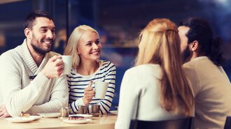 Vier Personen sitzen in einem von der offino Bürolösungen GmbH installierten Work-Café. Die Gesichter des Manns (schwarze Haare und Bart, weißer Wollpullover) und der Frau (blonde, lange Haare und dunkelblau-weiß-gestreiftes Longshirt) sind zu sehen – die der beiden anderen (lange rötliche Haare, graues Oberteil bzw. schwarze Haare mit Pferdeschwanz und schwarzem Bart, weißer Pullover) sind der Kamera abgewandt.